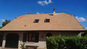 Maison avec un crépis rose et une toiture avec des tuiles oranges. Il y à deux fenêtres de toit et une cheminée.